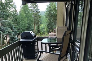 A balcony with a grill, a chair, and a view of a forest. - Interlude Condos by iTrip Aspen Snowmass (Snowmass Village)