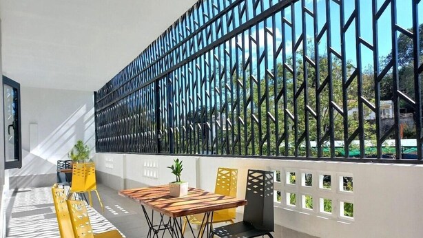 An outdoor seating area with a table and chairs, a potted plant, and a view through a patterned fence. - Richy Hotel (Da Lat)