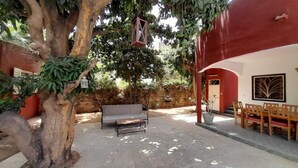 Une cour avec un banc, un coin repas avec des chaises et un arbre qui offre de l’ombre.