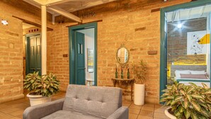 A lobby with a grey sofa, potted plants, a mirror, and a brick wall. - Botánica Casa Hotel (Medellín)