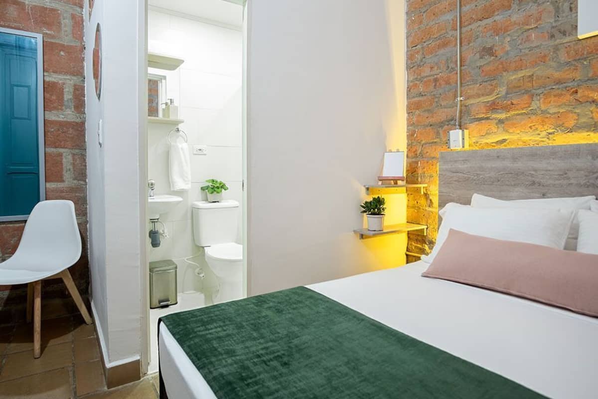 Un dormitorio con cama, una silla, baño y pared de ladrillo.