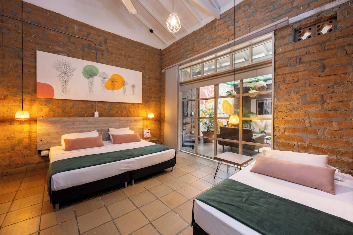 Una habitación de hotel con pared de ladrillo, un ventanal grande y una cama con edredón verde.