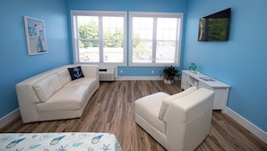 Una habitación con pared azul, un sofá blanco, un sillón blanco y una ventana con persianas.