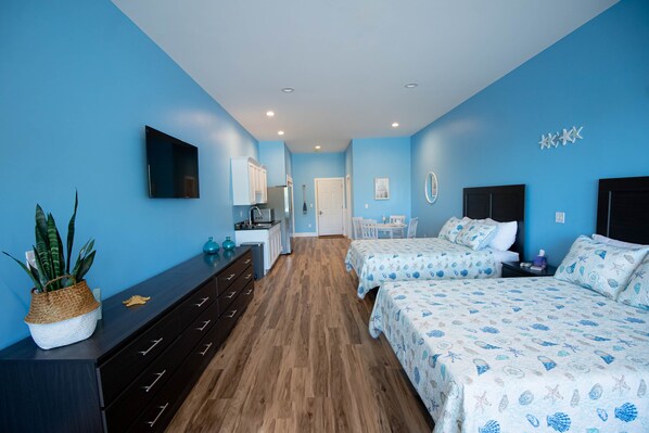 Une chambre avec deux lits, un bureau, une chaise, une commode et un téléviseur fixé au mur.