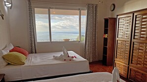 A hotel room with two beds, a large window with a view of the sea, a wooden wardrobe, and a small shelf with decorative items. - Villa Sea Forever, Big Ocean View, Heart of Manuel Antonio (Quepos)