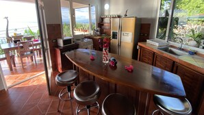 A kitchen with a large island, wooden cabinets, a refrigerator, and a view of the outdoors. - Villa Sea Forever, Big Ocean View, Heart of Manuel Antonio (Quepos)