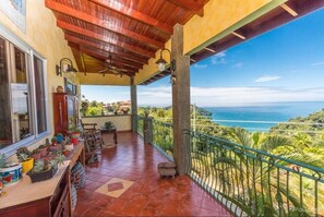 Un balcon abrité offrant une vue sur l’océan, agrémenté de plantes en pot et d’une table en bois.