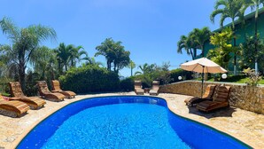 A swimming pool with lounge chairs and an umbrella, surrounded by palm trees and a stone wall. - Villa Sea Forever, Big Ocean View, Heart of Manuel Antonio (Quepos)