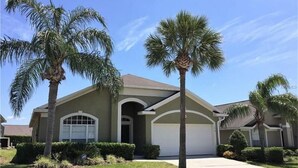 A two-story house with a garage, surrounded by well-maintained lawns and palm trees. - Glenbrook Lovely 4 Bed Pool/Spa Home! (Clermont)