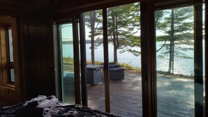 Een kamer met een grote schuifglazen deur die uitkomt op een terras met uitzicht op een meer en bomen.