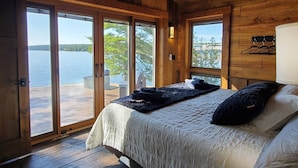 Een slaapkamer in een houten chalet met een bed, een groot raam en uitzicht op een meer.