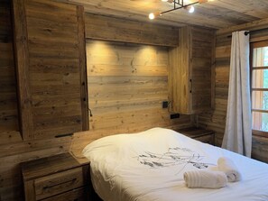 Una habitación tipo cabaña de madera con una cama, una mesita de noche y un ventanal con cortinas.