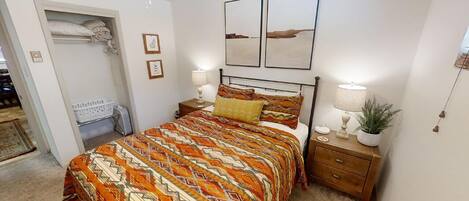 Una camera da letto con un letto, comodini, una lampada, una pianta e opere d'arte alle pareti.