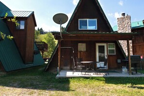 A wooden cabin with a sloped roof, a satellite dish, a small porch with chairs, and a stone chimney. - CJ A-Frame 2 - In Town - Ski In/Ski Out - On The River - Free WiFi (Red River)