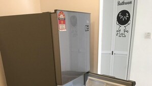 Een compacte koelkast met vriesvak, in een kamer met een houten vloer en een deur waarop 