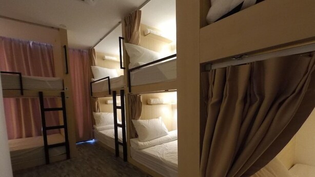 Een slaapkamer met stapelbed, houten vloer, een ladder en gordijnen.