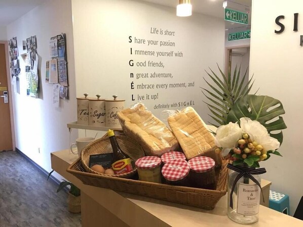 A reception area with a wall sign, a wicker basket with food items, a bottle, and a vase with flowers. - Signel Hostel (Kota Kinabalu)