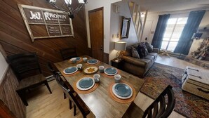 Une salle à manger avec une table en bois dressée pour six personnes, entourée de chaises. On peut voir un mur en bois avec une enseigne au-dessus de la table.