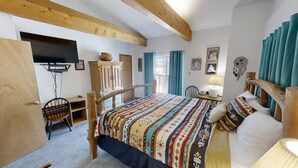 A bedroom with a bed, wooden headboard, a desk, a chair, a television, and a window with curtains. - LRM Cabin - In Town - Walk to Main Street - WiFi - Satellite - Wood Burning Fire (Red River)