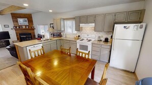 A compact kitchen with a wooden dining table, grey cabinets, and a white refrigerator. - LRM Cabin - In Town - Walk to Main Street - WiFi - Satellite - Wood Burning Fire (Red River)