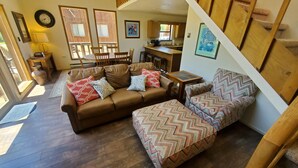 A cozy living room with a brown leather sofa, patterned ottoman, and a dining area with wooden chairs and a table. - Beaver Lodge - In Town - On the River - Near Copper Chair Lift - Free WiFi - Cab (Red River)
