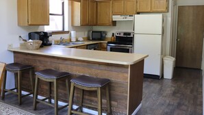 A kitchen with wooden cabinets, a built-in microwave, a stove, and a refrigerator. There are three stools at the counter. - Beaver Lodge - In Town - On the River - Near Copper Chair Lift - Free WiFi - Cab (Red River)