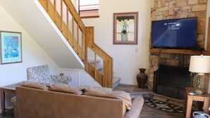 A living room with a brown leather sofa, a wooden staircase, a flat-screen TV mounted on a stone wall, and a fireplace. - Beaver Lodge - In Town - On the River - Near Copper Chair Lift - Free WiFi - Cab (Red River)