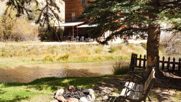 A rustic wooden cabin with a covered patio, a small pond, and a bench under a tree. - By the River - In Town - On The River - Backyard Fishing Spot - Free WiFi - Cabl (Red River)