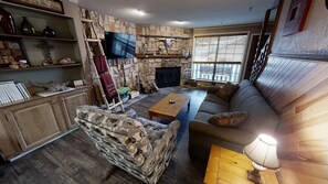 A cozy living room with a stone fireplace, a sofa, a coffee table, and a television mounted on the wall. - Rose Rock Mountain View - In Town - Pet Friendly - Wood Fireplace - Wifi - Washe (Red River)