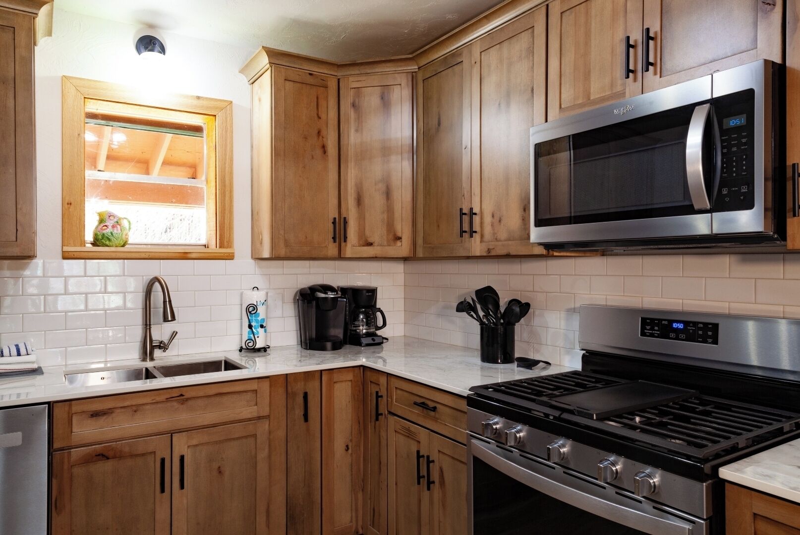 A modern kitchen with wooden cabinets, a stainless steel microwave, a gas stove, and a coffee maker.
