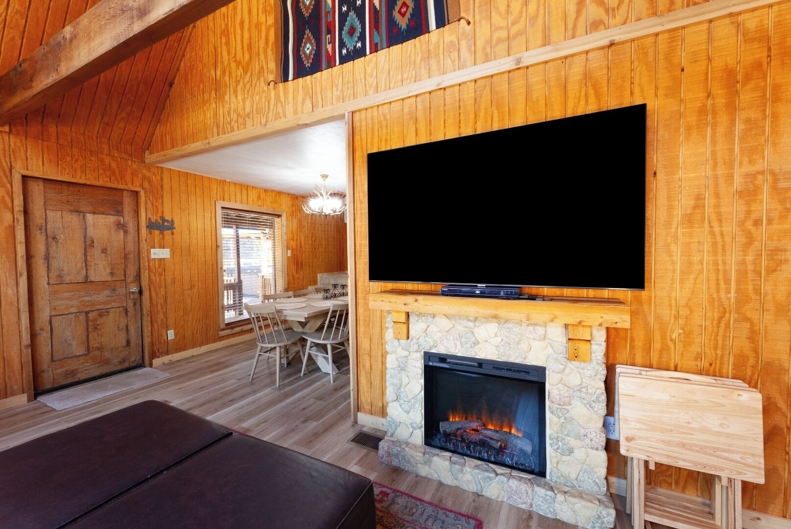 L’intérieur d’un chalet accueillant, avec une cheminée en pierre, un téléviseur fixé au-dessus et un coin repas comprenant une table et des chaises.