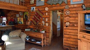 A log cabin interior with a cozy living area, wooden walls, and various decorative items including paintings, a fish sculpture, and woven baskets. - Dwyer's Den - Upper Valley - Rustic Interior and Decor - Near The River - Satell (Red River)