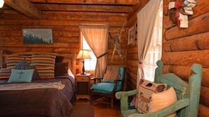 A cozy log cabin room with a bed, a chair, a nightstand, and a lamp. - Dwyer's Den - Upper Valley - Rustic Interior and Decor - Near The River - Satell (Red River)