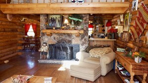 A cozy log cabin interior with a stone fireplace, a dining area, and a living room with a sofa and a coffee table. - Dwyer's Den - Upper Valley - Rustic Interior and Decor - Near The River - Satell (Red River)