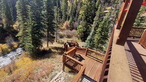 A wooden deck with a view of a forested area and a stream.