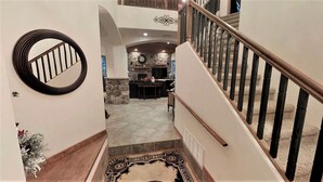 A staircase leading to a living area with a stone fireplace, a round mirror, and a patterned rug.