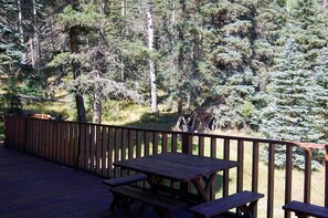 Eine Holzterrasse mit Picknicktischen und Geländer, mit Blick auf einen bewaldeten Bereich.