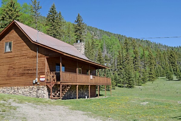 Eine Holzhütte mit Veranda, Stein Fundament und Blick auf einen bewaldeten Hang.