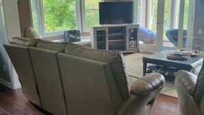 En stue med en stor hjørnesofa, et fladskærms-tv på et træstel og en skydedør, der fører ud til en balkon.