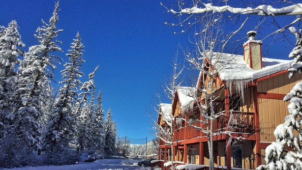 A snow-covered wooden building with a balcony, surrounded by snow-laden trees.