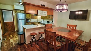 A kitchen with wooden cabinets, a built-in refrigerator, a dining table with four chairs, and a bar stool area.