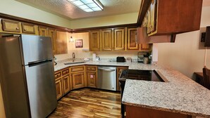 A kitchen with wooden cabinets, a stainless steel refrigerator, a dishwasher, granite countertops, and a wooden floor.