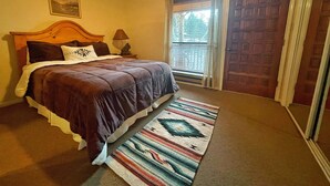 Un dormitorio con una cama de madera, una mesita de noche, una lámpara, una ventana con persianas y una puerta.