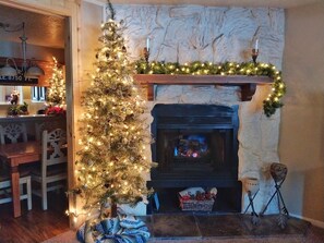 A cozy living room with a fireplace, a decorated Christmas tree, and a stone wall.
