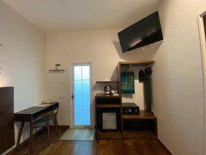 A compact room with a desk, chair, a flat-screen TV mounted on the wall, a microwave, and a small cabinet.