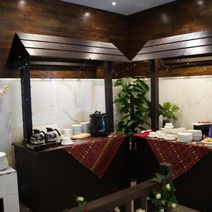 A buffet setup with a central serving area, a coffee station, and a large potted plant.