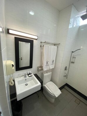A modern bathroom with a white sink, mirror, and toilet, a towel rack with towels, and a shower area.