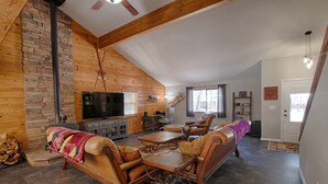 A cozy living room with a stone fireplace, wooden ceiling beams, a television, and leather furniture. - Mountain Living at its Finest! (Pinetop)