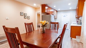 A dining room with a wooden table and chairs, a vase with flowers, and wooden cabinets.