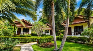 Un hotel de estilo cabaña con jardín, palmeras y cielo despejado.